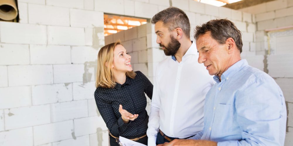 Young couple with architect or civil engineer looking at plans of their new house, discussing issues at the construction site.